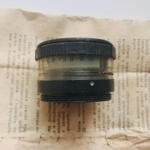 K&ouml;nnte beinhalten: Ein schwarzes und transparentes Kameraobjektiv mit dem Text "16 11 8 56 42" auf der Seite.