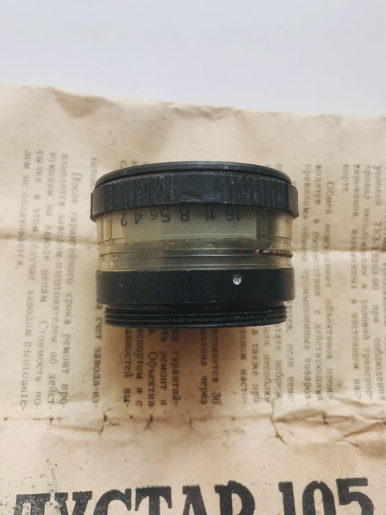 K&ouml;nnte beinhalten: Ein schwarzes und transparentes Kameraobjektiv mit dem Text "16 11 8 56 42" auf der Seite.