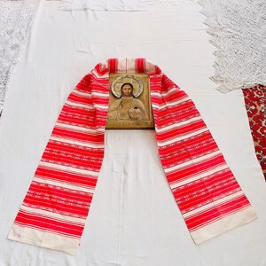 May include: A red and white striped fabric with a religious icon of Jesus Christ in the center. The fabric is folded in half and laid out on a white surface.