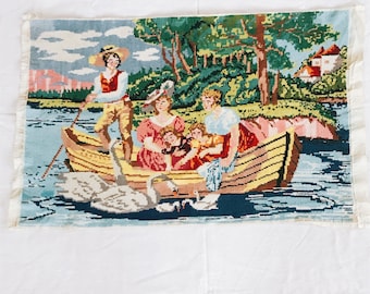 May include: A colorful needlepoint picture of a family in a boat on a lake. The boat is yellow and the family is dressed in colorful clothing. There are two swans swimming in the water.