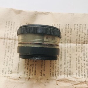 K&ouml;nnte beinhalten: Ein schwarzes und transparentes Kameraobjektiv mit der Nummer "64 2.8" auf der Seite. Das Objektiv ist ein Vintage-Kamerateil.