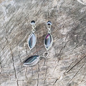 May include: A set of three silver earrings and a pendant featuring iridescent black stones in a teardrop shape.