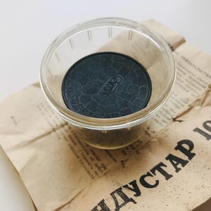 K&ouml;nnte beinhalten: Ein schwarzer Gummideckel mit einer strukturierten Oberfl&auml;che und dem aufgedruckten Wort "INDUSTAR". Der Deckel befindet sich in einem durchsichtigen Glasgef&auml;&szlig;.