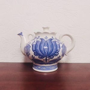 以下が含まれることがあります： 青と白の花柄の白いティーポット。ティーポットは丸いボディで、左側に注ぎ口があります。ハンドルは右側にあります。