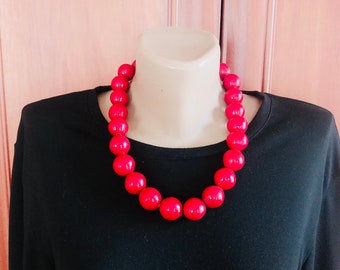 Può includere: Una collana di perle rosse con grandi perle rotonde. La collana è su un manichino che indossa una camicia nera.
