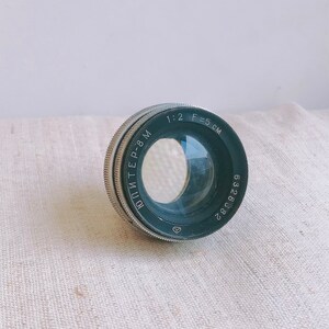 以下が含まれることがあります： 縁に「Jupiter-8 M 1:2 F=5 CM 6328002」と印刷された黒と銀のカメラレンズです。