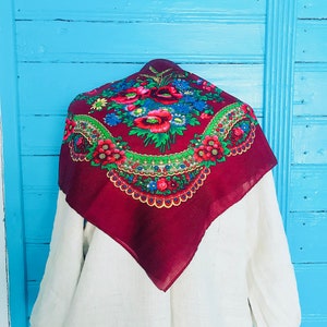 Puede incluir: Un pañuelo de cabeza rojo y blanco con estampado floral y borde festoneado. El pañuelo está drapeado sobre una camisa de lino blanca.