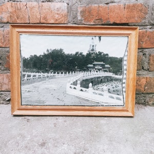 May include: A framed black and white photograph of a bridge with a pagoda in the background. The bridge is made of stone and has a white railing. The pagoda is tall and has a pointed roof. The photograph is in a wooden frame.