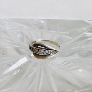 May include: A silver ring with a band that curves and twists, set with a row of small clear stones.