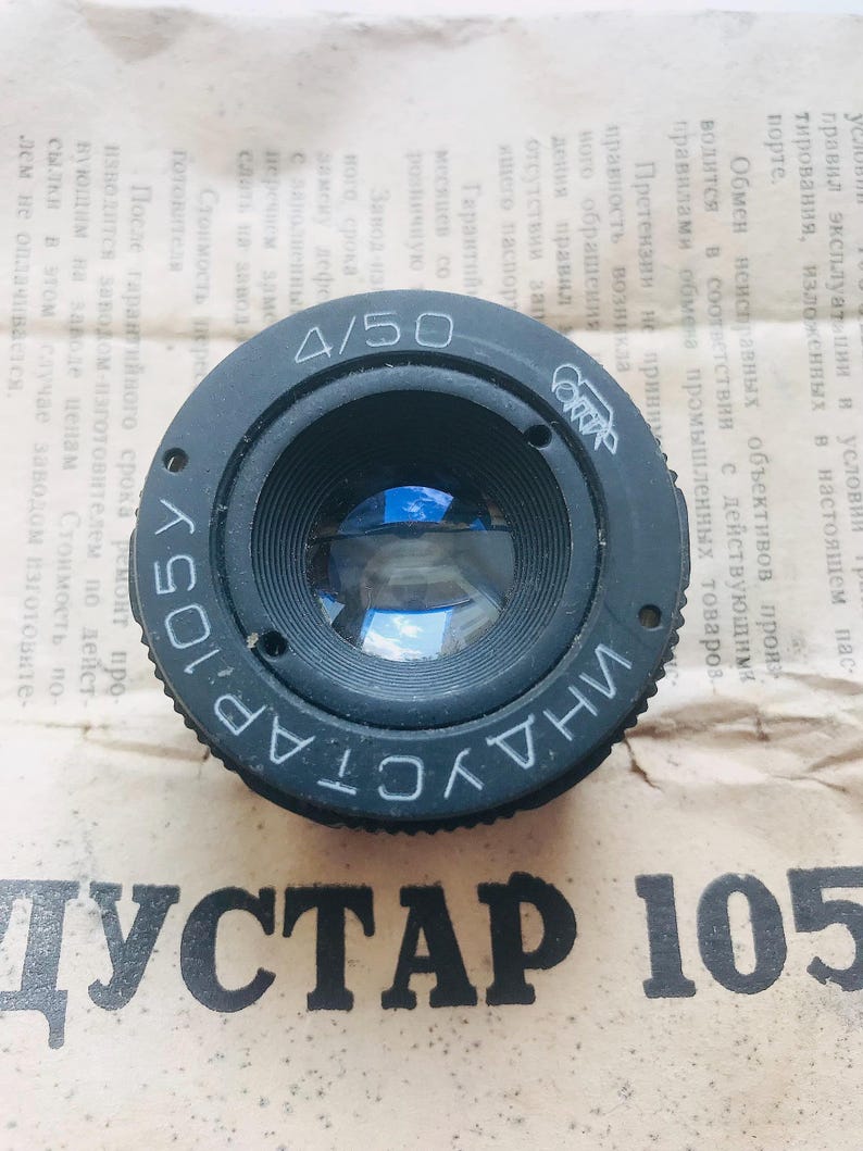 K&ouml;nnte beinhalten: Ein schwarzes Kameraobjektiv mit dem Text "INDUSTAR 105" und "4/50" auf der Seite. Das Objektiv hat ein blaues Glaselement, das durch die &Ouml;ffnung sichtbar ist.