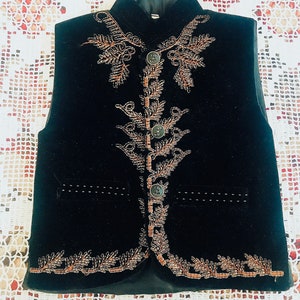 Op de afbeelding: Een zwart fluwelen vest met een mandarijnsluiting en ingewikkelde gouden borduursels. De borduursels hebben een bloemmotief met parelmoeraccenten.