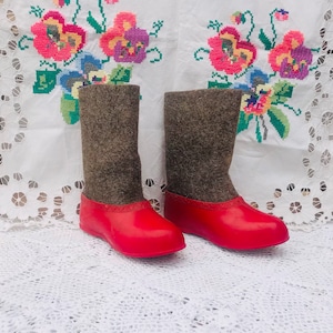 Puede incluir: Un par de botas de fieltro rojo con forro de piel marrón. Las botas están sobre un mantel blanco con flores bordadas.