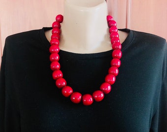 Può includere: Una collana di perle rosse con grandi perle rotonde. La collana è su un manichino che indossa una camicia nera.