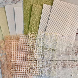 May include: A collection of handmade paper sheets in various textures and colors. The assortment includes shades of green, cream, and peach, with patterns like grid, netting, and textured surfaces. Ideal for crafting and art projects.