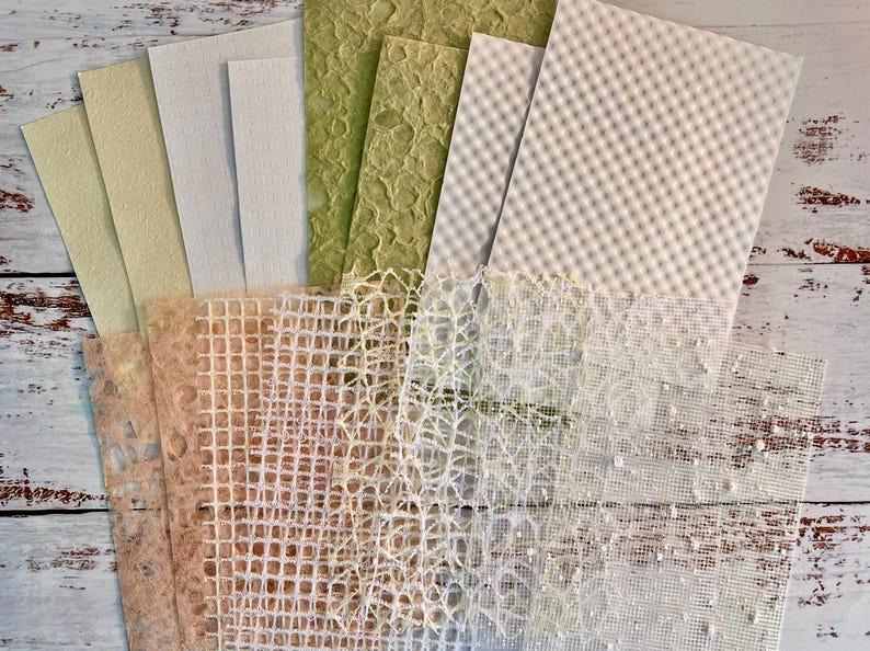 May include: A collection of handmade paper sheets in various textures and colors. The assortment includes shades of green, cream, and peach, with patterns like grid, netting, and textured surfaces. Ideal for crafting and art projects.