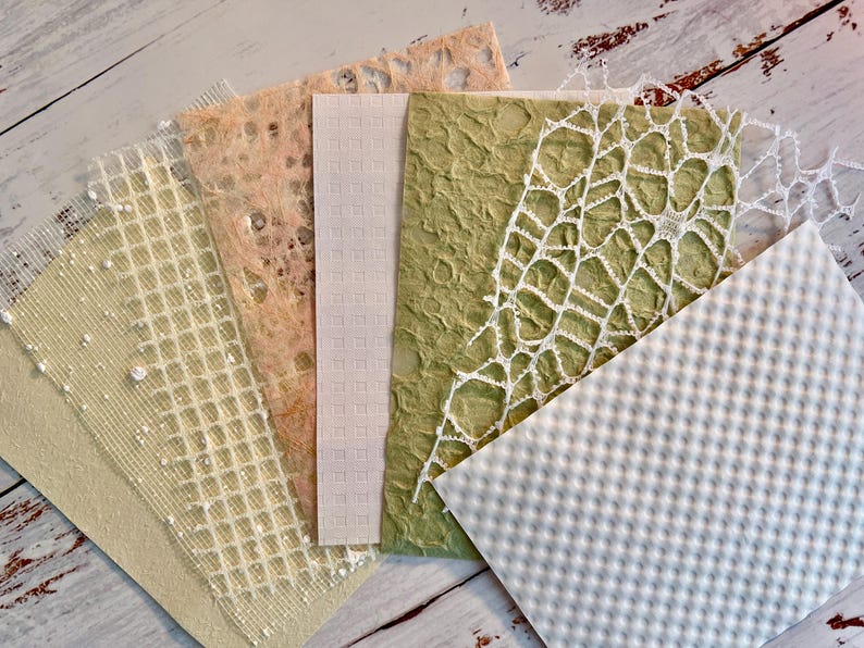 May include: A collection of handmade paper samples in various textures and colors. The samples include a light green paper with a textured surface, a white paper with a grid pattern, and a peach-colored paper with a delicate, open weave.