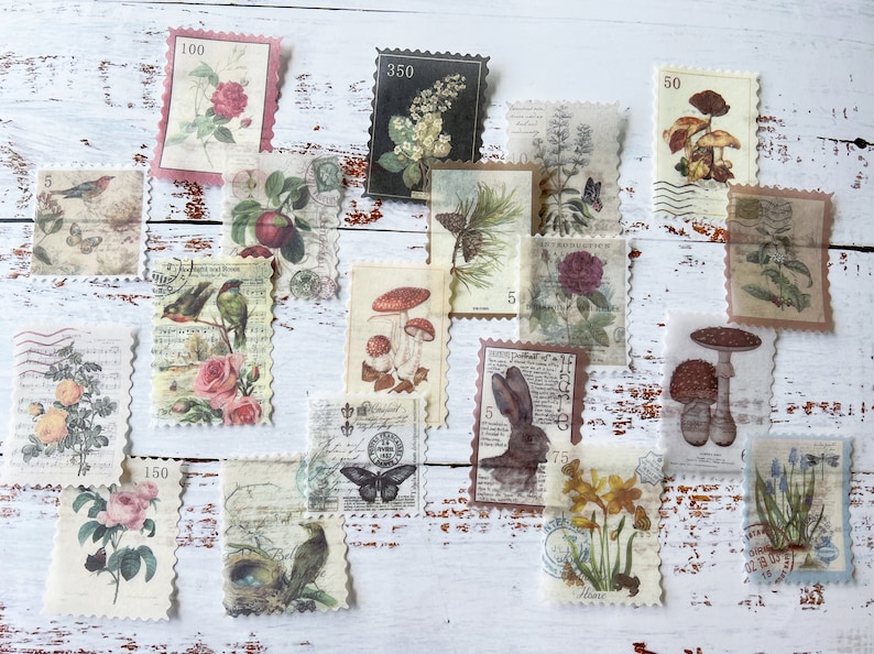 May include: A collection of vintage-style postage stamps featuring botanical and nature illustrations. The stamps showcase images of flowers, birds, mushrooms, and a rabbit, with varying denominations and decorative borders. The stamps are arranged on a white wooden surface.