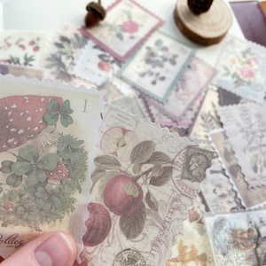 May include: A collection of vintage-style paper stamps with botanical and nature-themed illustrations. The stamps feature images of mushrooms, apples, flowers, and other natural elements in soft, muted colors. The stamps have a scalloped edge and are slightly translucent.