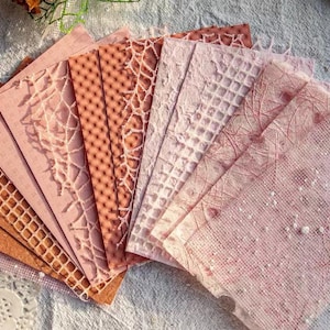 May include: A collection of patterned paper sheets in shades of pink and brown. The papers feature various textures, including lace, geometric patterns, and speckled designs. Ideal for scrapbooking, card making, or other paper crafts.