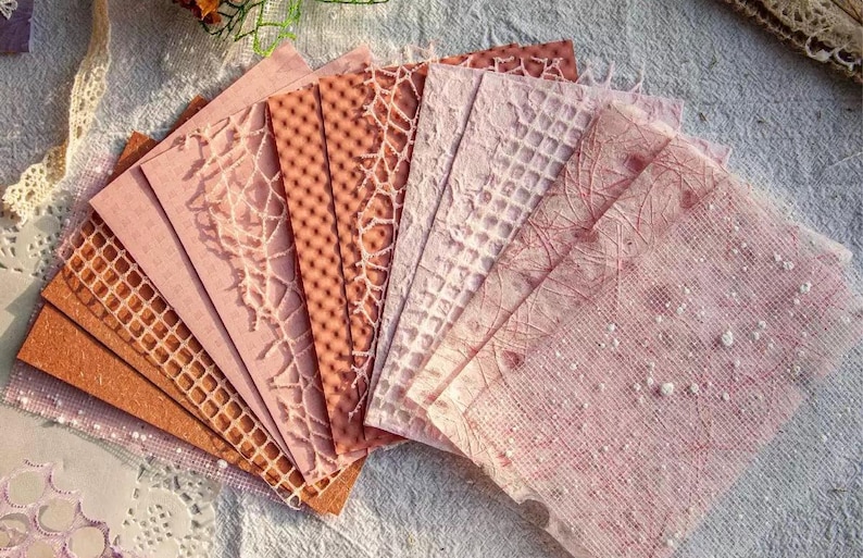 May include: A collection of patterned paper sheets in shades of pink and brown. The papers feature various textures, including lace, geometric patterns, and speckled designs. Ideal for scrapbooking, card making, or other paper crafts.