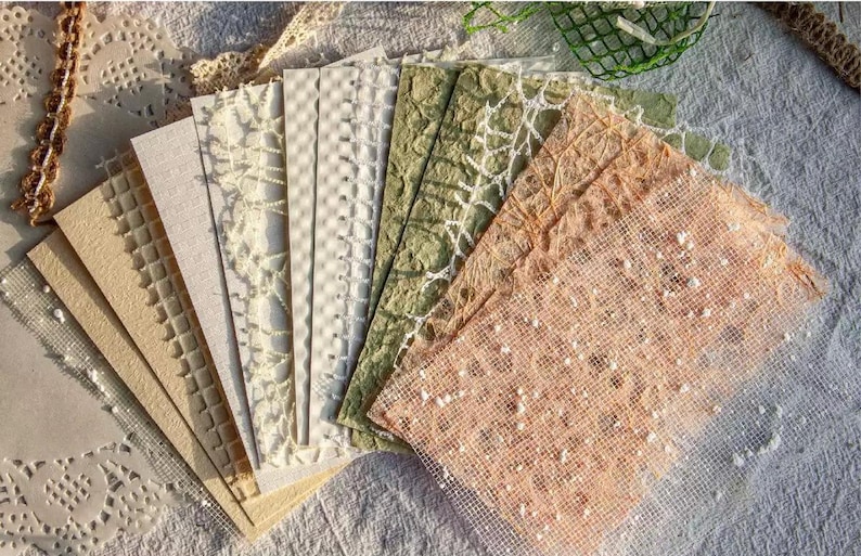 May include: A collection of textured paper sheets in various colors, including beige, cream, and green. The papers have different patterns, such as lattice, grid, and floral designs. The papers are arranged in a fan shape, showcasing their unique textures.