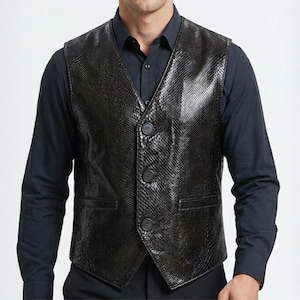 May include: A black vest featuring a textured snakeskin pattern, a V-neckline, and three front buttons. The garment is worn over a solid black long-sleeved button-down shirt. The vest includes two horizontal welt pockets on the lower front panels.