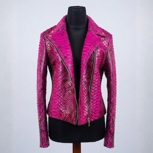 May include: A vibrant magenta motorcycle jacket featuring a textured snakeskin pattern throughout. The jacket includes a notched collar, an asymmetrical front zipper closure, and long sleeves with zippered cuffs, all finished with metallic gold hardware.