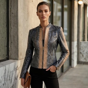 May include: A stylish, snakeskin-patterned jacket in shades of blue and tan, featuring a front zipper and long sleeves. The jacket is paired with black pants and a brown clutch. The overall look is fashionable and sophisticated.