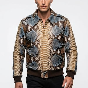 May include: A snakeskin-patterned bomber jacket in shades of brown, tan, and blue. The jacket features a collared neckline, two front pockets, and a brown ribbed hem and cuffs. The model is wearing black pants.
