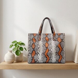 Orange snakeskin tote bag displayed on wooden shelf with minimalist decor