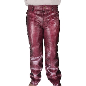 Puede incluir: Un pantalón de piel de serpiente de color burdeos. El pantalón tiene una pierna recta y una cremallera.
