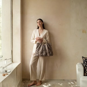 May include: A white ceramic mug with a black handle and the text "But First, Coffee" in a bold, black font. The mug is set against a blurred background, suggesting a cozy setting.