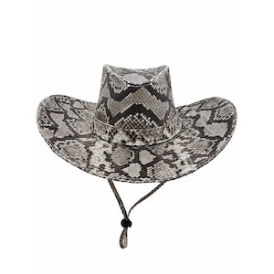 Puede incluir: Un sombrero de vaquero con un patrón de piel de serpiente en tonos gris, negro y blanco en toda la copa y el ala. El sombrero incluye una correa para la barbilla a juego con textura de piel de serpiente y un cierre de cordón negro ajustable.