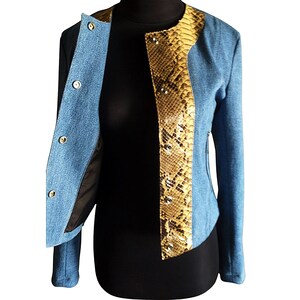 Op de afbeelding: Een blauw denim jack met een slangenskin paneel aan de voorkant. Het jack heeft een ritssluiting en een opstaande kraag.