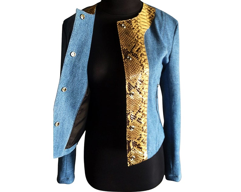 Op de afbeelding: Een blauw denim jack met een slangenskin paneel aan de voorkant. Het jack heeft een ritssluiting en een opstaande kraag.