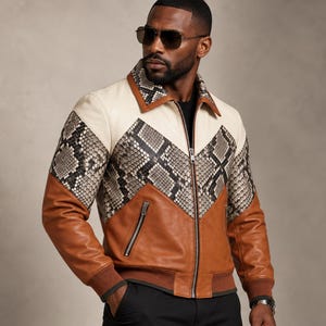 May include: A leather bomber jacket featuring a cream-coloured upper chest and collar, a central chevron-shaped panel with a grey and black snakeskin pattern, and solid brown leather sleeves and lower body with a ribbed brown hem and cuffs.