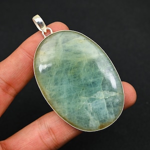 Puede incluir: Un colgante de plata con una gran piedra de aguamarina de forma ovalada. La piedra tiene un color azul verdoso claro y una apariencia translúcida.