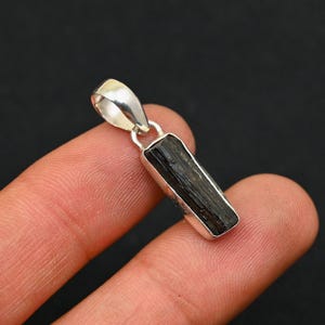 以下が含まれることがあります： 黒いトルマリンの宝石が付いたシルバーペンダント。ペンダントは長方形で、滑らかで磨かれた仕上げになっています。