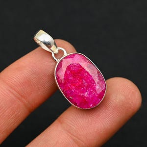 Op de afbeelding: Een zilveren hanger met een grote, ovale robijn edelsteen. De robijn is een diepe, levendige roze kleur en heeft een licht getextureerd oppervlak.