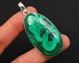 May include: A green malachite gemstone pendant with intricate swirling patterns, set in a silver oval frame.