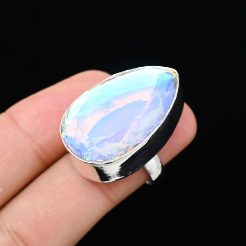 Puede incluir: Anillo de plata con una gran piedra preciosa iridiscente en forma de pera. La piedra muestra una gama de colores, incluyendo azul, morado y amarillo. El anillo est&aacute; sobre un fondo oscuro.