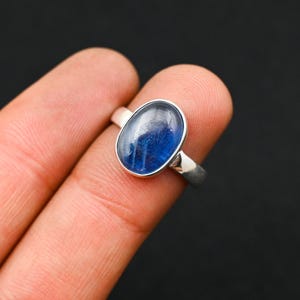 May include: A silver ring with a blue oval gemstone. The ring is on a finger.