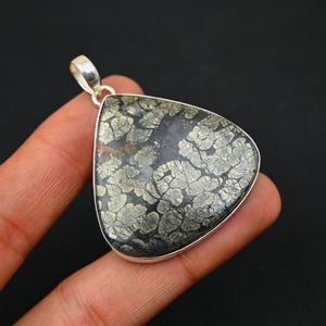 Könnte beinhalten: Ein silberner Anhänger mit einem dreieckigen, dunkelgrauen Stein, der ein einzigartiges, filigranes Muster aus silbernen und goldenen Flecken aufweist.