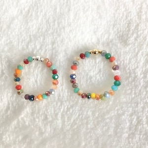 Könnte beinhalten: Zwei bunte Perlenringe, einer mit einem goldenen Verschluss und einer mit einem silbernen Verschluss. Die Perlen sind eine Mischung aus Rot, Orange, Gelb, Grün, Blau und Lila.