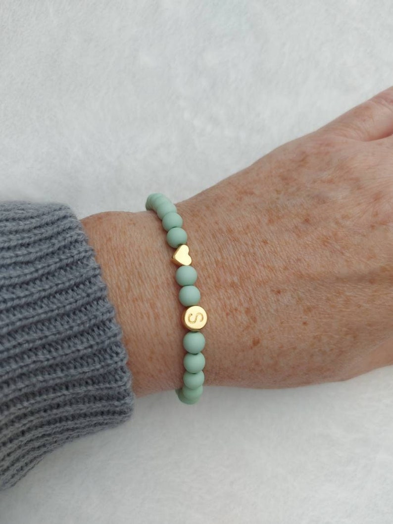 Puede incluir: Un brazalete de cuentas verde menta con un dije de coraz&oacute;n dorado y un dije de letra 'S' dorado.