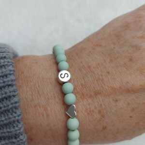 Puede incluir: Un brazalete de cuentas de color verde claro con un dije de plata que dice "S" y un dije de coraz&oacute;n de plata.