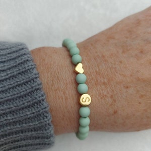 Puede incluir: Un brazalete de cuentas verde menta con un dije de coraz&oacute;n dorado y un dije de letra 'S' dorado.