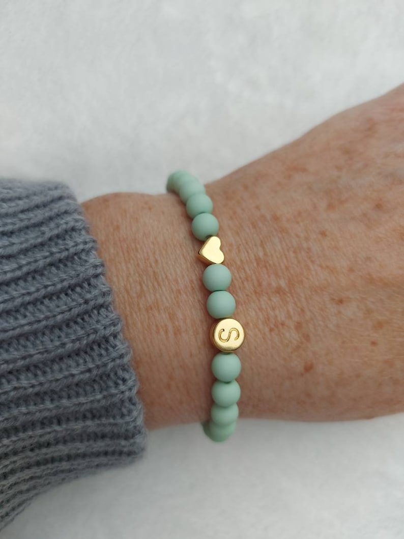 Puede incluir: Un brazalete de cuentas verde menta con un dije de coraz&oacute;n dorado y un dije de letra 'S' dorado.