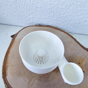 Op de afbeelding: Witte keramische plantenbak met een ingebouwd waterreservoir. De plantenbak heeft een afvoergaten en een klein zijvak voor het vasthouden van water.