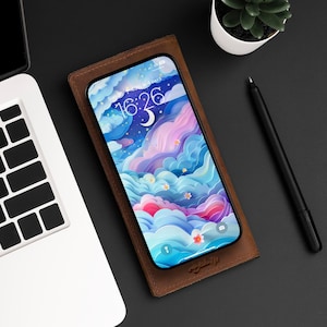 Puede incluir: Una funda de teléfono de cuero marrón con un teléfono inteligente en su interior. La pantalla del teléfono muestra un diseño abstracto colorido con nubes y estrellas. La hora es 16:26.